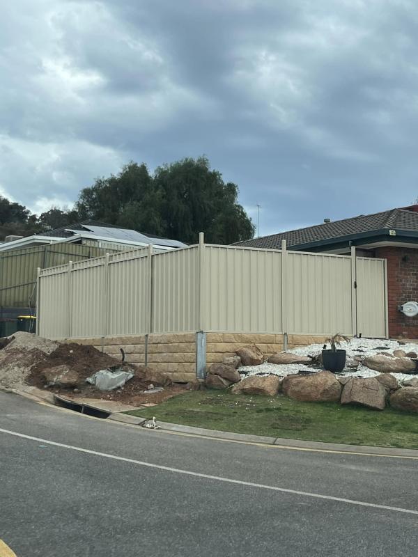 Cream Colorbond fence on a sandstone retaining wall, with high posts run for electrical lighting